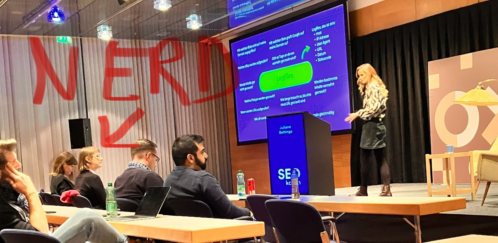 Juliane Bettinga präsentiert auf der SEOkomm in Salzburg 2024 zum Thema Logfile Analyse Light mit den GSC Crawl Stats. Sabine Langmann im Publikum ist, laut Pfeil und Text im Bild, ein Nerd.