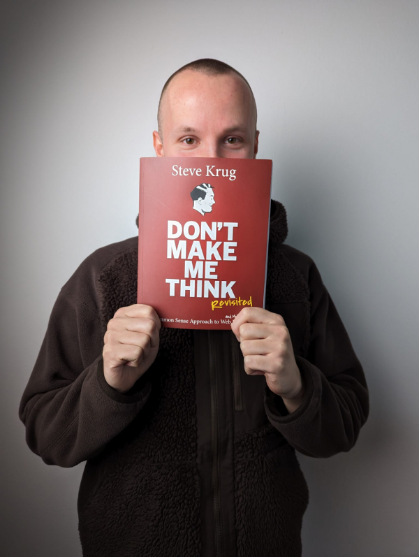Ein Foto von Philipp, wie er das Buch "Don't make me think" von Steve Krug in den Händen vor seinem Gesicht hält, sodass man nur den Bereich ab den Augen sehen kann.
